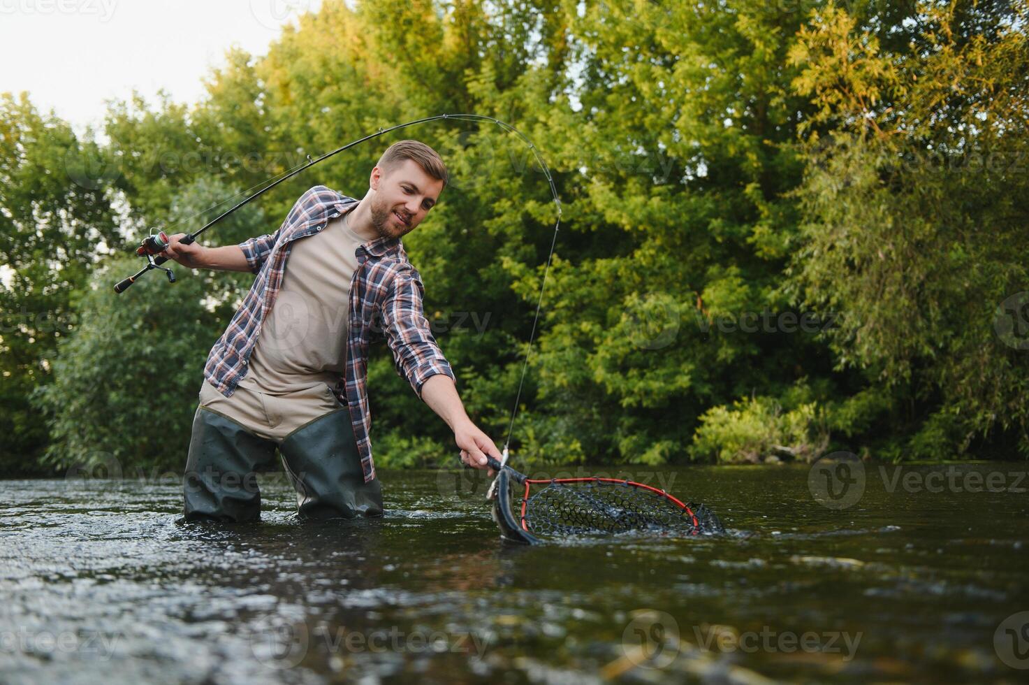 uomo con pesca asta, pescatore uomini nel fiume acqua all'aperto. attraente trota pesce nel rete. estate pesca passatempo foto