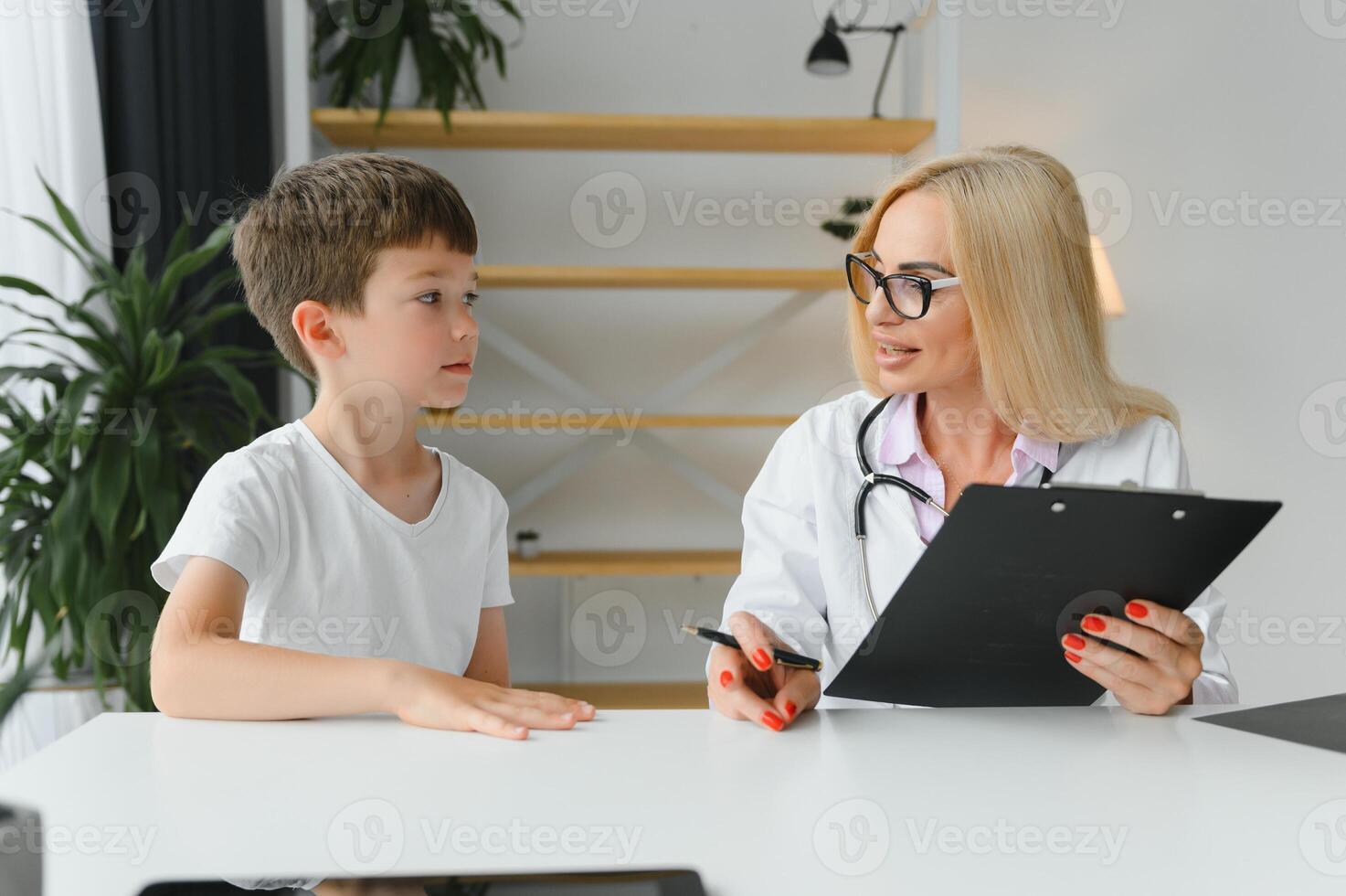 sorridente giovane femmina medico o pediatra parlare comfort piccolo ragazzo paziente a consultazione nel privato clinica. cura donna gp supporto rallegrare poco ragazzo esaminare consultare nel Ospedale. assistenza sanitaria concetto. foto