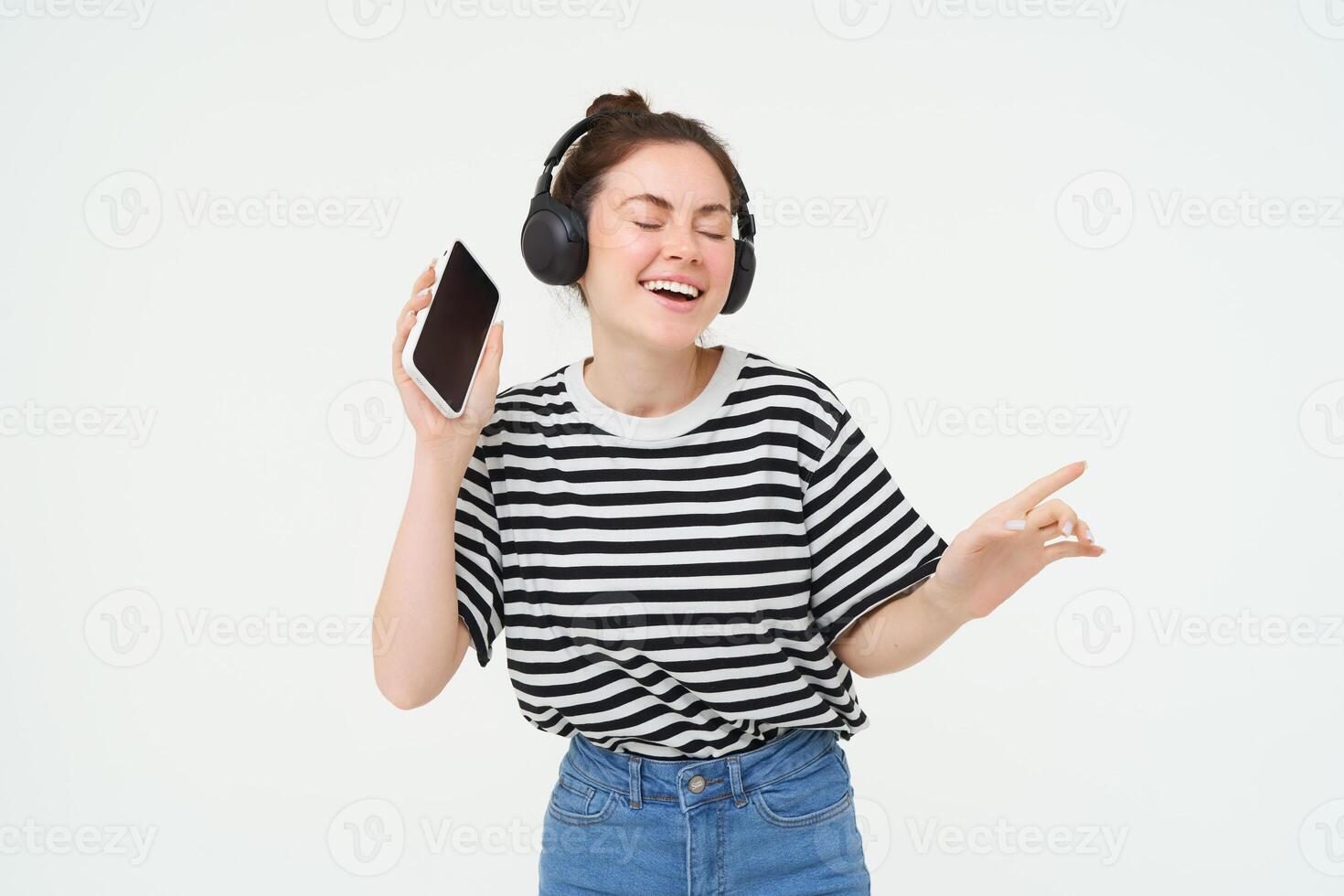 ragazza con smartphone ballare, ascoltando per musica nel senza fili cuffia, utilizzando mobile Telefono streaming App per godere preferito canzoni, isolato al di sopra di bianca sfondo foto