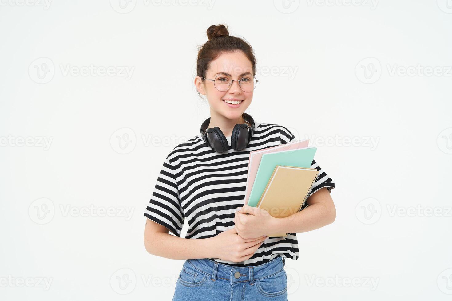 formazione scolastica concetto. sorridente brunetta ragazza, alunno nel casuale Abiti, detiene sua libri, studia Materiale, indossa cuffie al di sopra di collo, sembra fiducioso e felice, isolato al di sopra di bianca sfondo foto