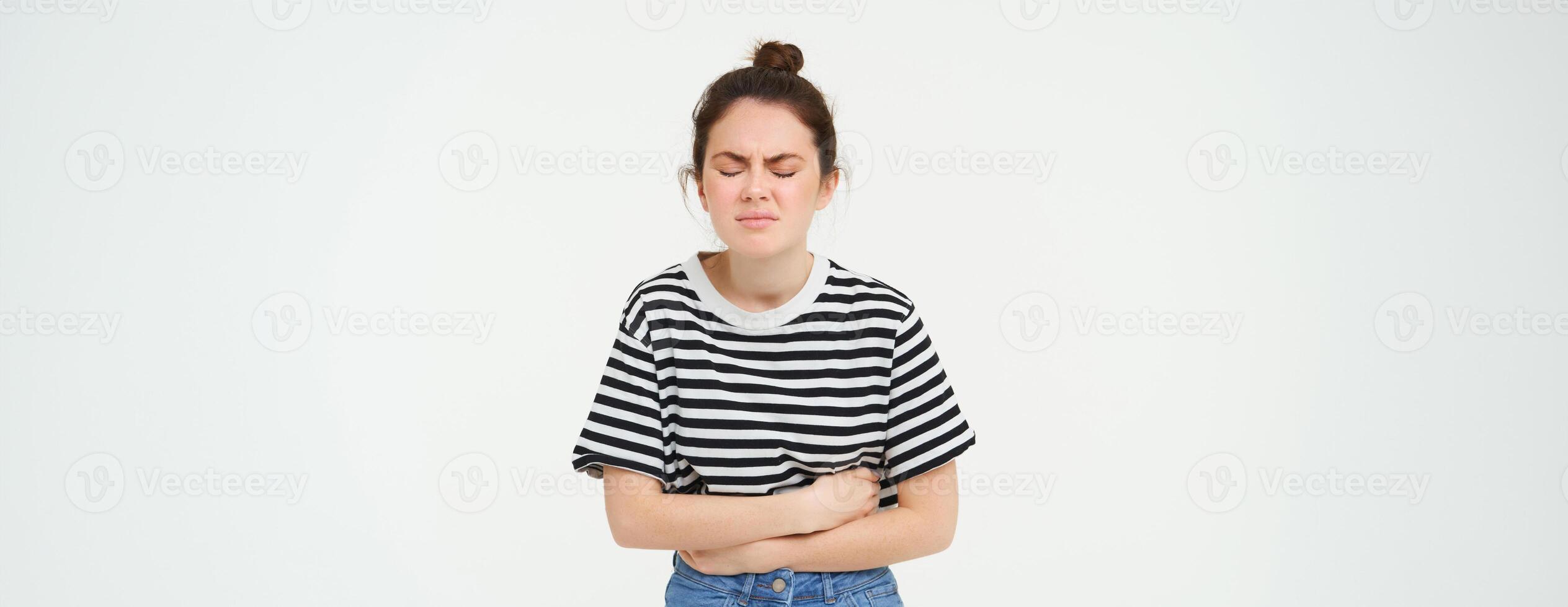 ritratto di donna smorfie a partire dal doloroso mestruale crampi, tocchi sua gonfiarsi, disagio o stomaco dolore, sta al di sopra di bianca sfondo foto