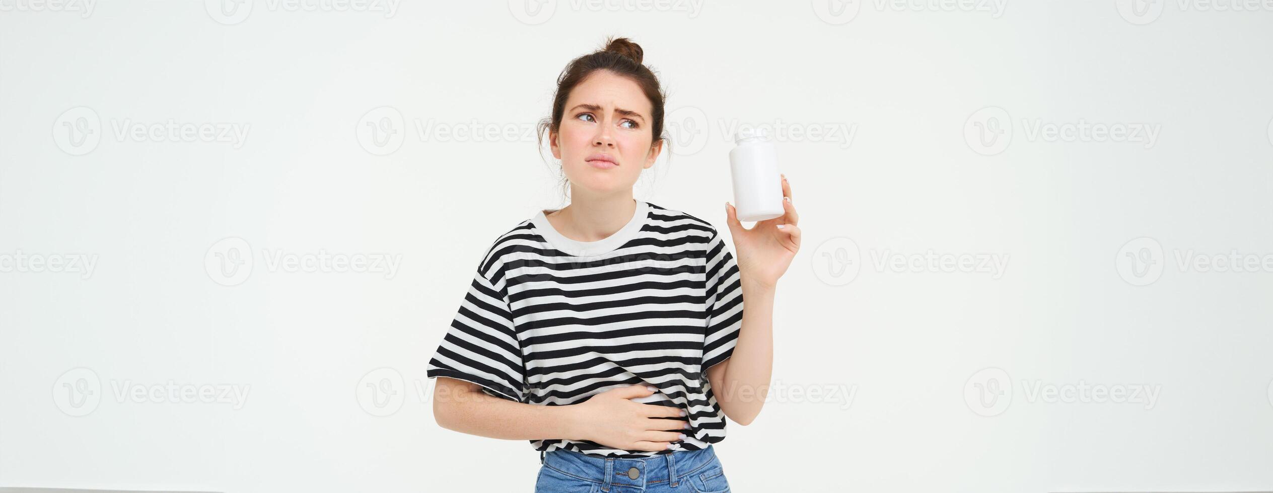 Immagine di donna con stomaco dolore, Spettacoli bottiglia con pillole, prende tavoletta a partire dal mestruale crampi, periodo dolore, calmante disagio, in piedi al di sopra di bianca sfondo foto