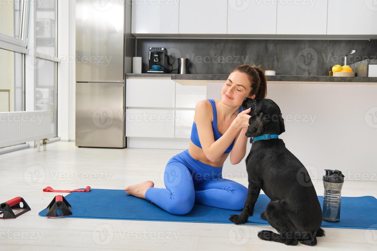 ritratto di bellissimo brunetta fitness ragazza, giochi con sua cane durante allenarsi formazione sessione, si siede a casa su gomma da cancellare yoga stuoia, fa sport esercizi nel vivente camera foto