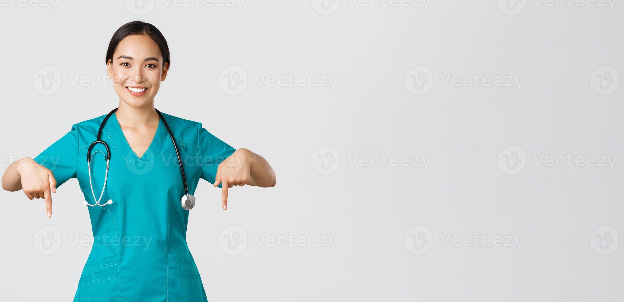 covid19, assistenza sanitaria lavoratori, pandemia concetto. sorridente piacevole asiatico femmina medico, terapista o medico nel scrub con stetoscopio, puntamento dita fuori uso, mostrare clinica bandiera foto