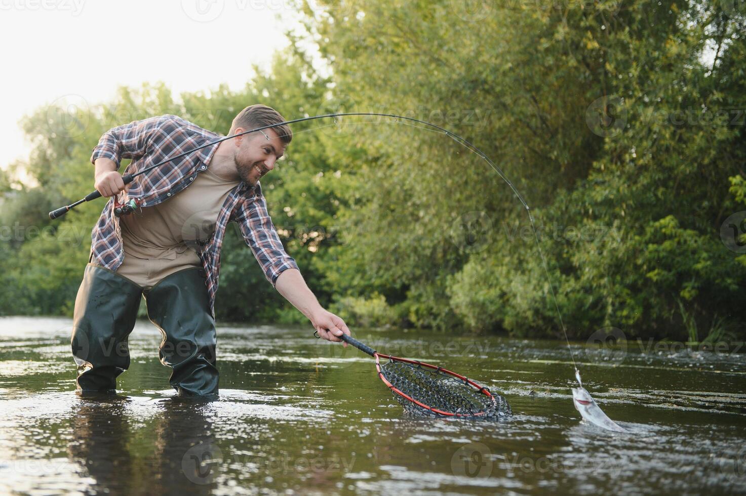 uomo con pesca asta, pescatore uomini nel fiume acqua all'aperto. attraente trota pesce nel rete. estate pesca passatempo foto