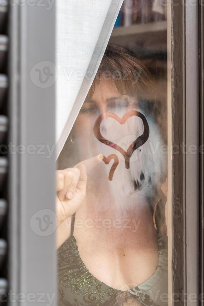 contento e nel amore donna disegno un' cuore forma su il bicchiere di un' finestra di sua Casa foto