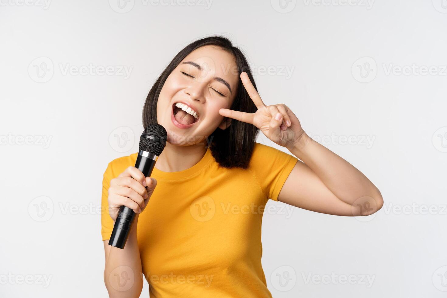 contento asiatico ragazza danza e cantando karaoke, Tenere microfono nel mano, avendo divertimento, in piedi al di sopra di bianca sfondo foto