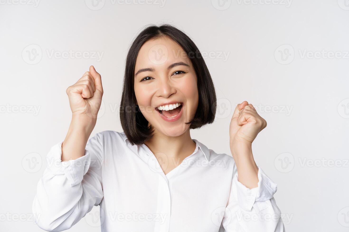 vicino su viso ritratto di danza asiatico donna sorridente, trionfante e festeggiare con contento emozione, in piedi al di sopra di bianca sfondo foto