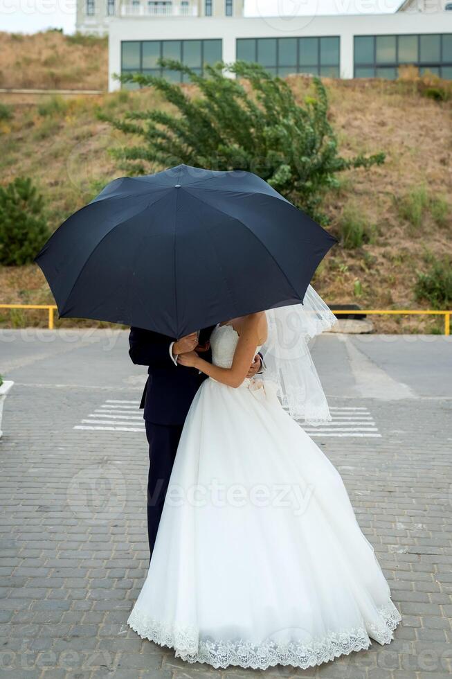 sposa e sposo a nozze giorno a piedi all'aperto. bridal coppia, contento sposini donna e uomo sotto ombrello. amorevole nozze avvicinamento. foto
