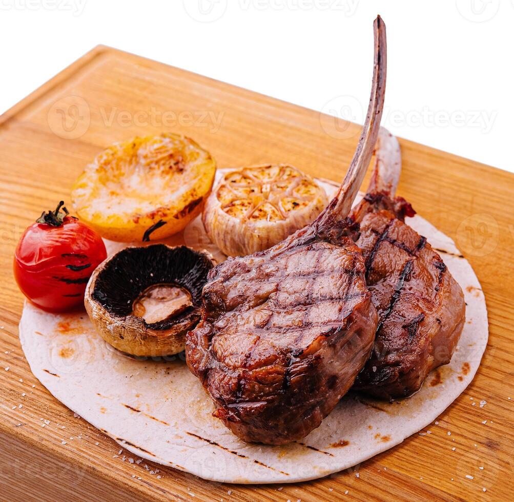 grigliato agnello braciole su di legno tavola con erbe aromatiche e spezie foto