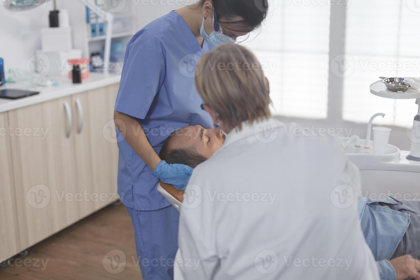 clinico ortodontista squadra con viso maschera l'esame paziente bocca durante medico chirurgia nel stomatologiche ufficio camera. anziano donna medico utilizzando professionale odontoiatria utensili per cavità procedura foto