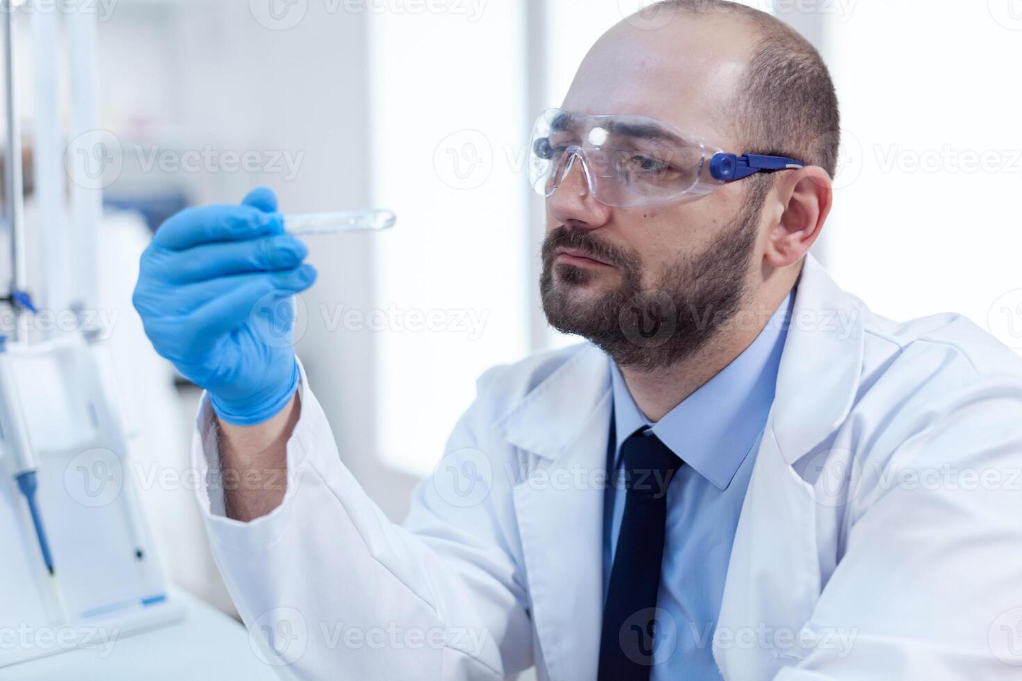 chimico scienziato detiene test tubo di bicchiere nel il suo mano per medicina sperimentare. ricercatore nel biotecnologia sterile laboratorio Tenere analisi nel tubo indossare guanti e protezione occhiali. foto