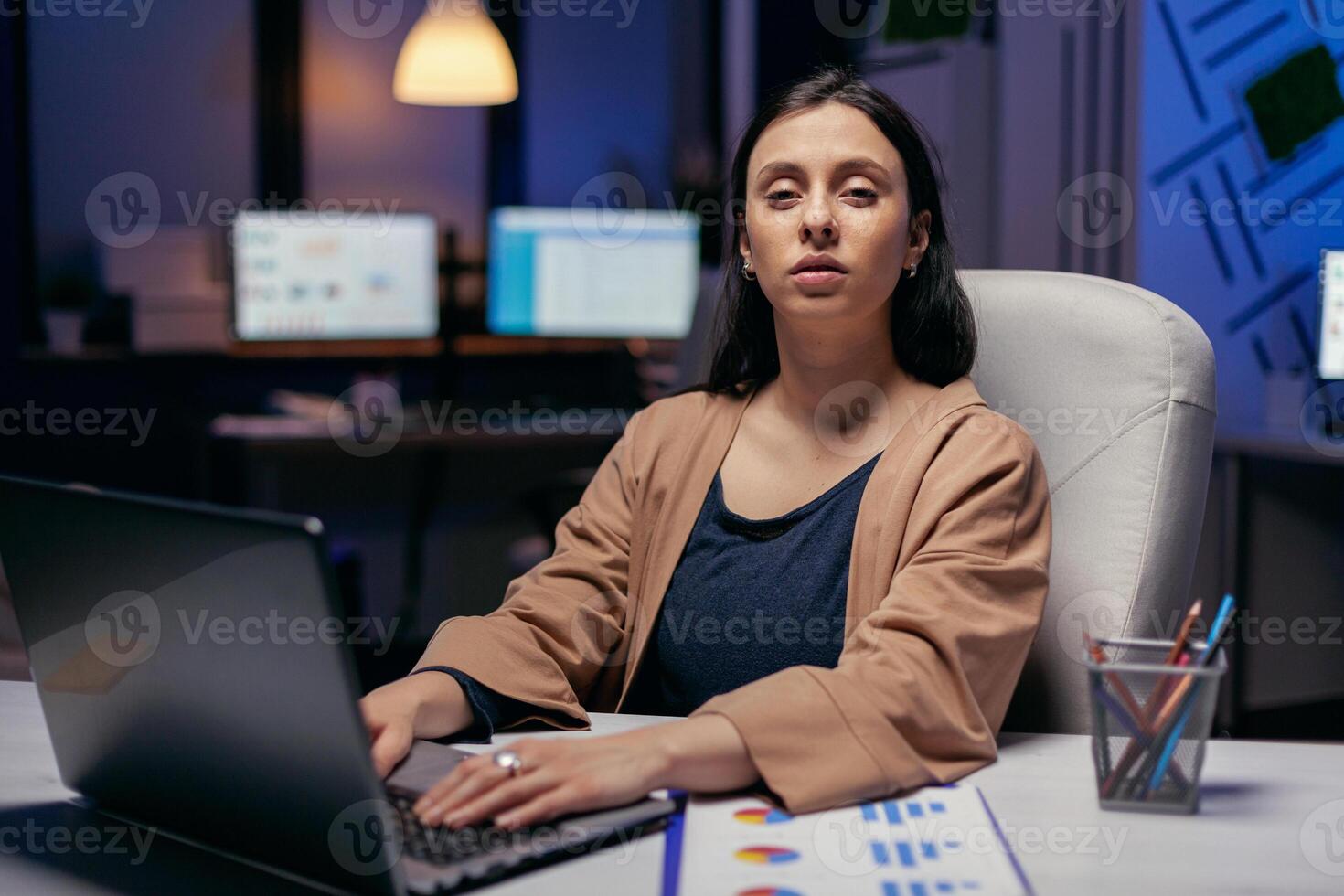 donna d'affari Tenere mani su il computer portatile tastiera guardare a telecamera. inteligente donna seduta a sua posto di lavoro nel il corso di in ritardo notte ore fare sua lavoro. foto