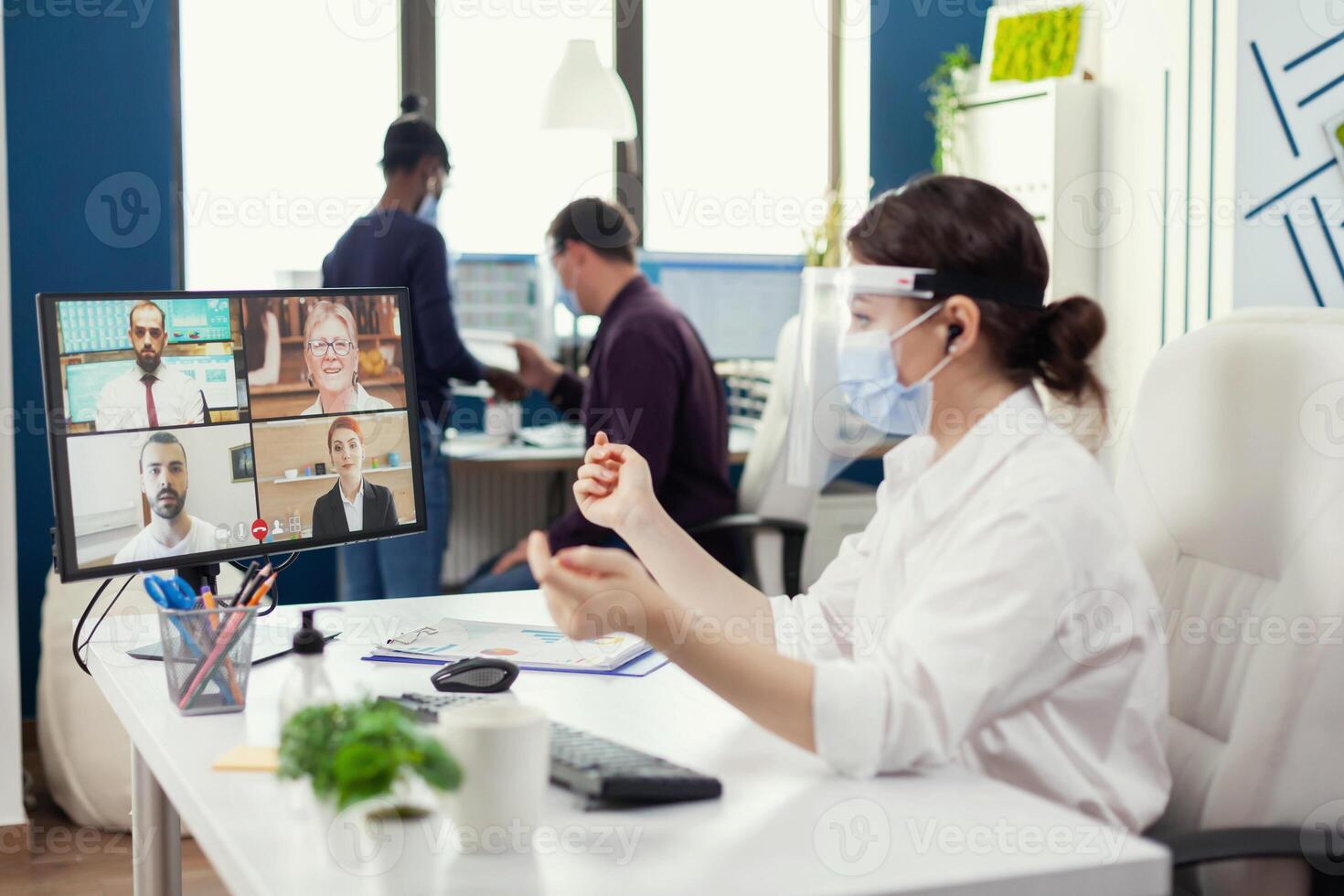 donna d'affari ascoltando uomini d'affari durante in linea conferenza su computer a posto di lavoro e indossare viso maschera. imprenditore avendo video chiamata mentre colleghi Lavorando rispetto sociale distanza durante globale pandemia. foto