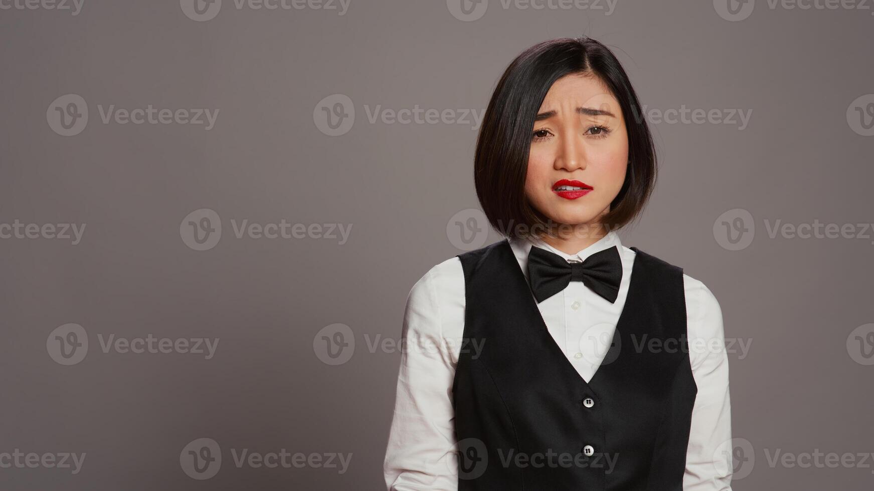 annoiato addetto alla reception essere confuso e oberati di lavoro nel studio, in posa con confusione e fatica al di sopra di grigio sfondo. asiatico amministratore sensazione incerto e insicuro di qualche cosa. telecamera b. foto