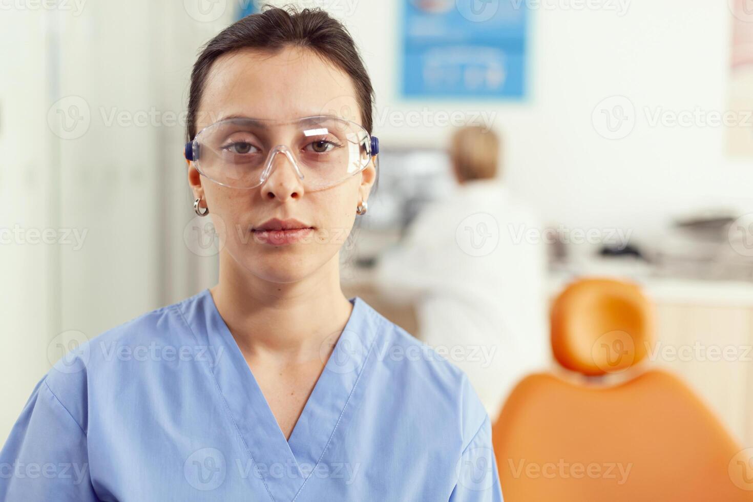 vicino su di donna infermiera nel uniforme guardare in telecamera mentre Lavorando nel stomatologia ospedale ufficio. medico squadra in attesa malato paziente per inizio dentale chirurgia durante stomatologiche appuntamento foto