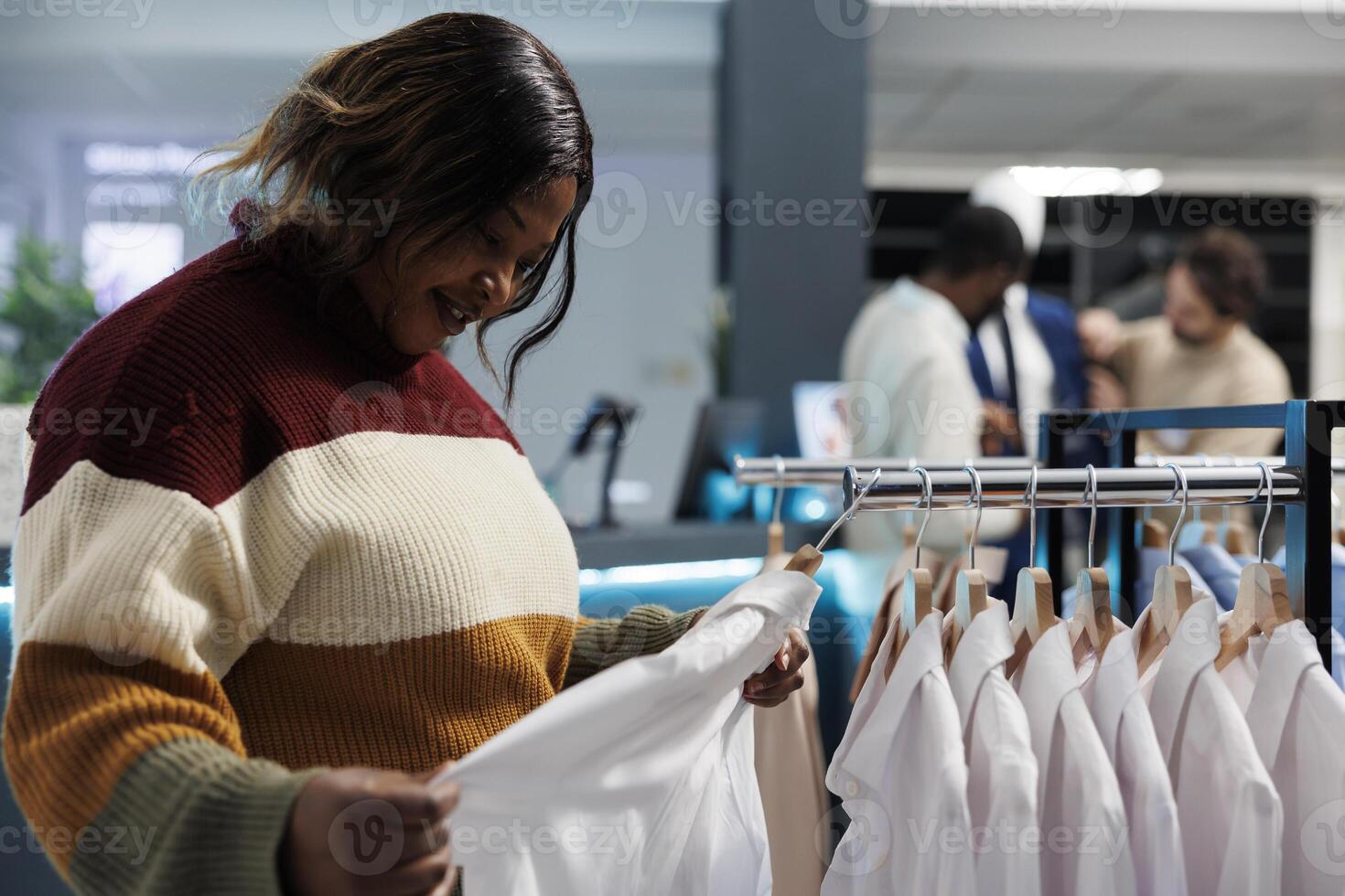 capi di abbigliamento memorizzare acquirente l'esame bianca camicia tessuto qualità, controllo in forma. africano americano donna navigazione cremagliera con sospeso formale indossare e Selezione abbigliamento dimensione nel boutique foto