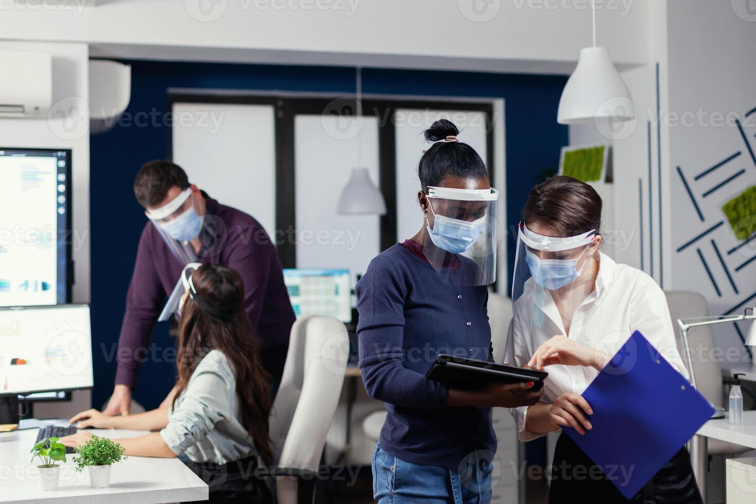 internazionale gruppo di persone Lavorando e comunicare in piedi a posto di lavoro indossare viso maschera contro covid19. multietnico attività commerciale squadra Lavorando rispetto sociale distanza durante globale pandemia con coronavirus. foto