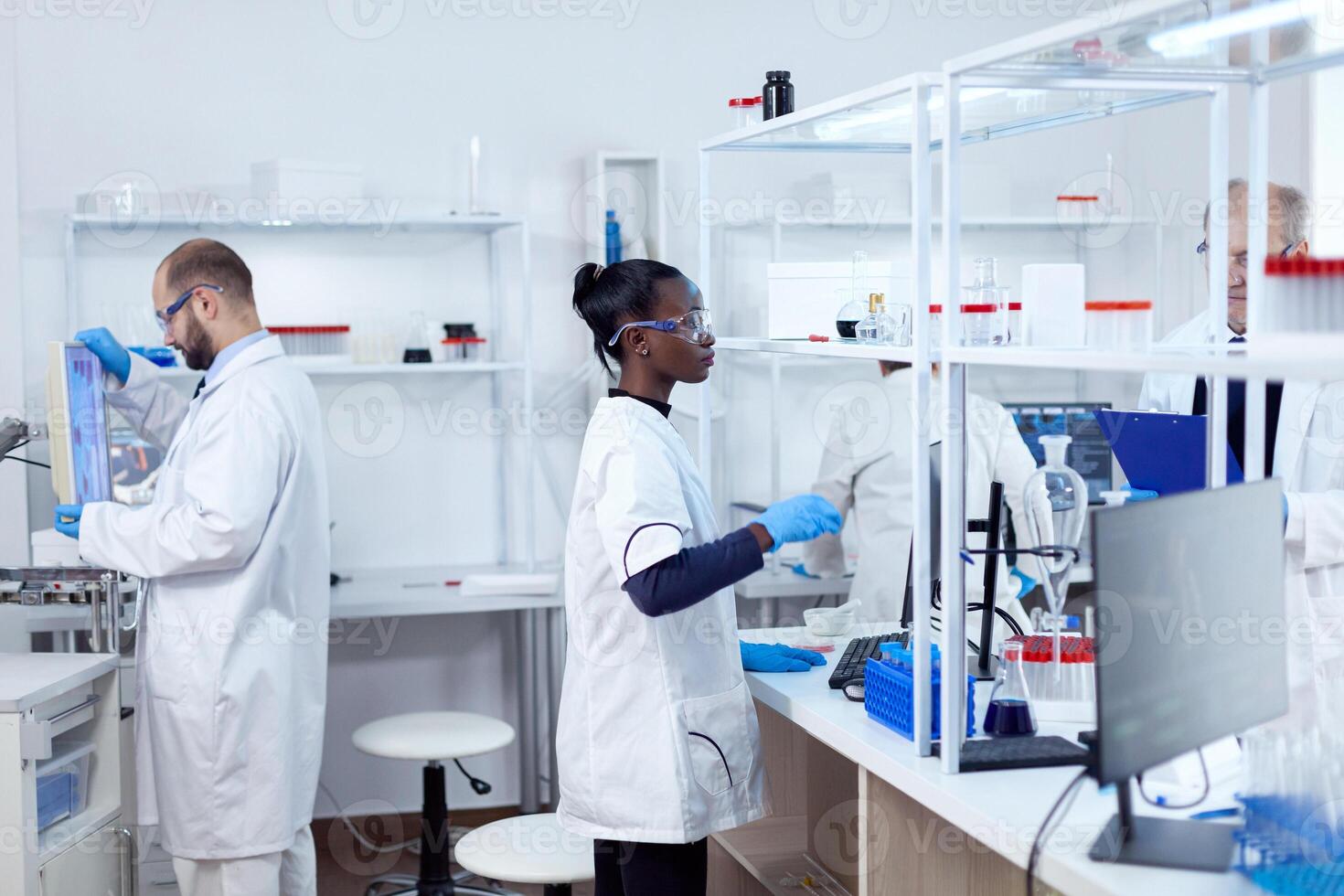 africano scienziato utilizzando bicchiere borraccia nel sterile microbiologia laboratorio per scoprire un' vaccino. multietnico squadra di ricercatori Lavorando nel laboratorio analisi soluzione per medico scopo. foto