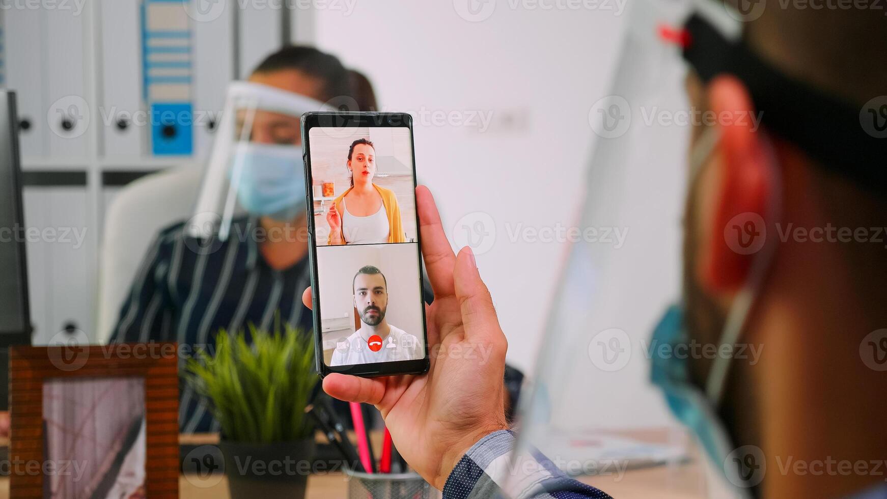 uomo d'affari capo conduce lontano comunicazione utilizzando smartphone per videoincontro parlando con remoto dipendente seduta nel nuovo normale ufficio aziendale costruzione. libero professionista rispetto sociale distanza foto