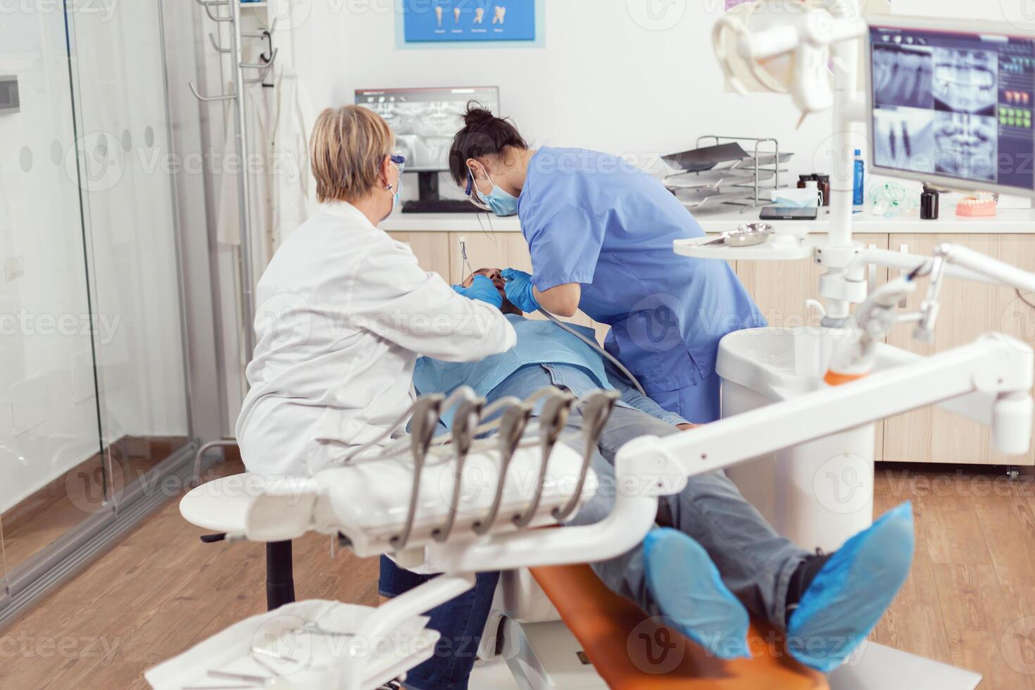 stomatologo anziano donna fare igienico pulizia di denti utilizzando sterile dentale Strumenti. paziente seduta con Aperto bocca su dentale sedia, dentista medico l'esecuzione visita medica nel moderno clinica foto