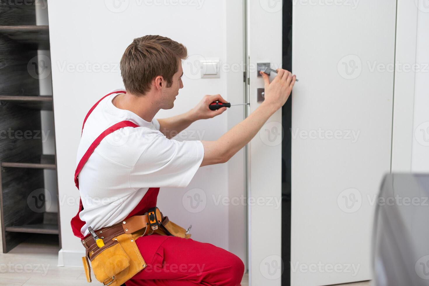 riparazione servizio concetto. ritratto di sorridente bello giovane fabbro ferraio nel blu uniforme installazione porta pomello su davanti di legno Ingresso porta a casa o ufficio posto di lavoro. foto