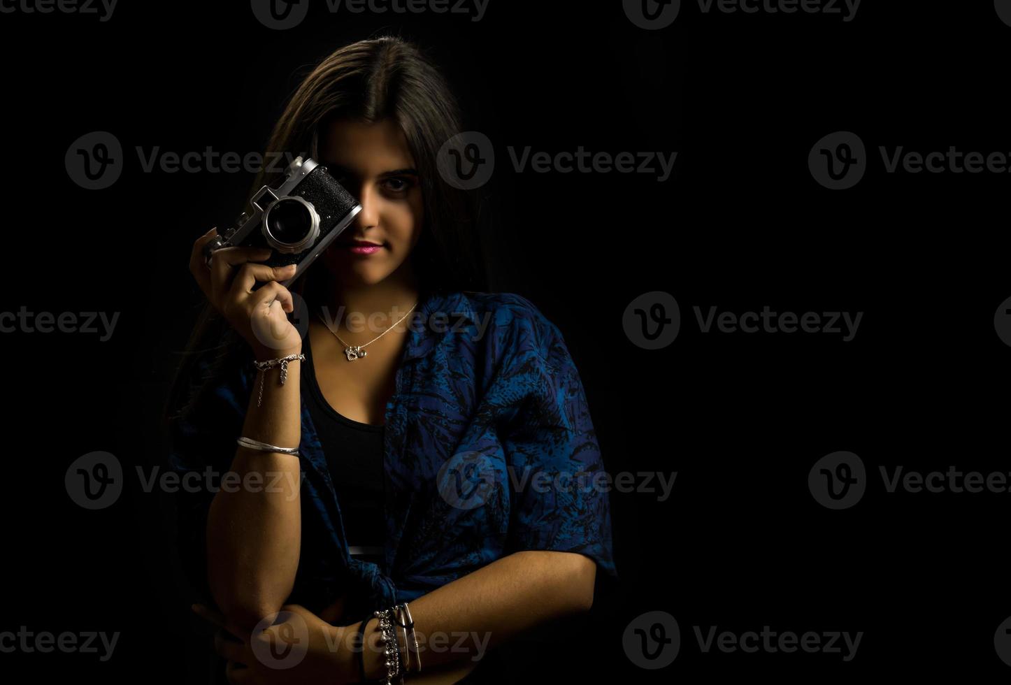 giovane ragazza in posa con una vecchia reflex, sfondo nero foto