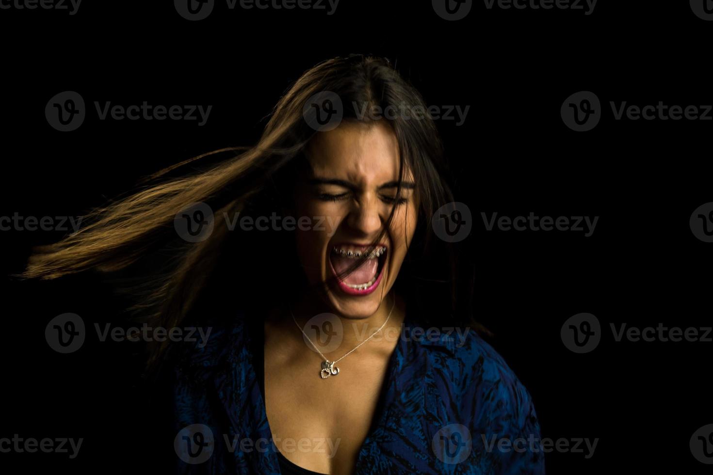 giovane ragazza bruna con lunghi capelli lisci che urla arrabbiato, sfondo nero foto