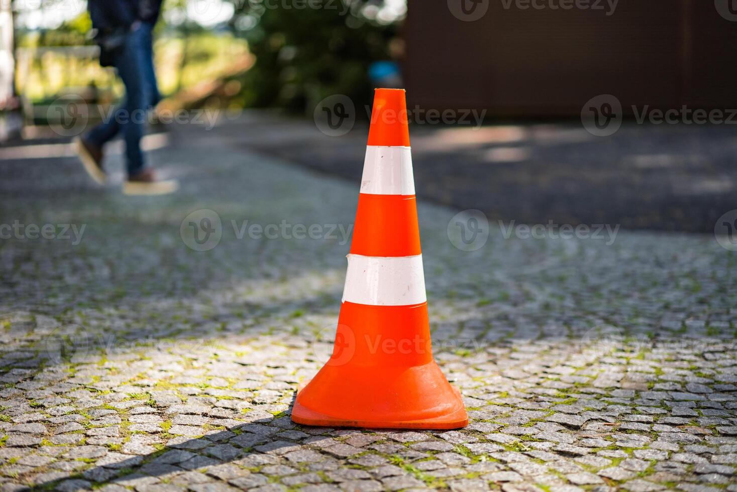 plastica arancia parcheggio cono in piedi nel il strada su il sfocato sfondo di maschi gambe. a strisce strada cartello per parcheggio nel il marciapiede. avvicinamento foto