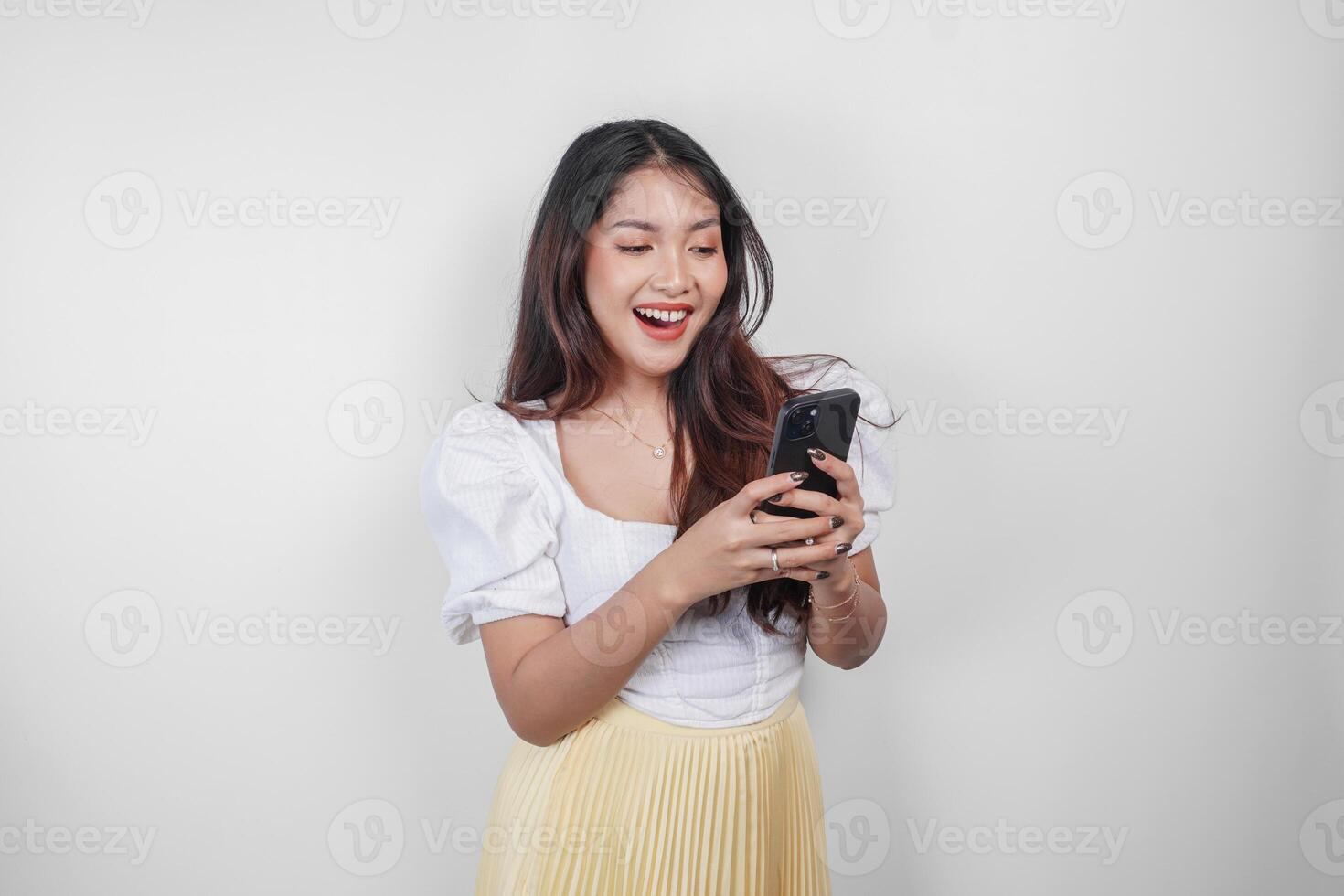 un' allegro asiatico donna è sorridente e Tenere sua smartphone, isolato di bianca sfondo. foto