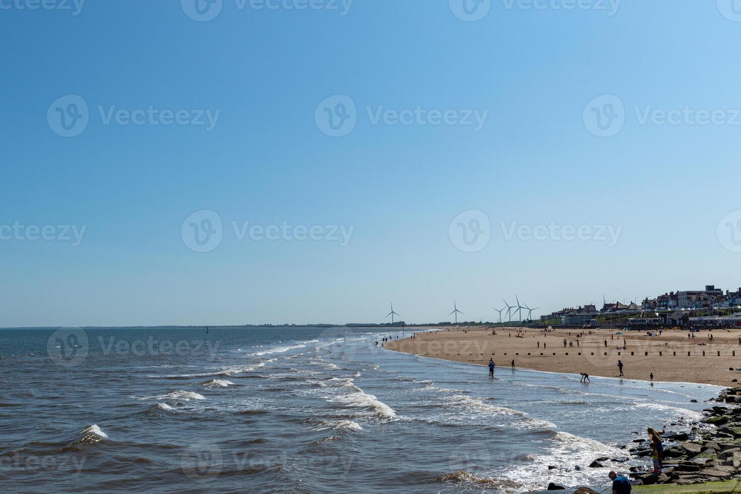 soleggiato beachscape con onde, sabbioso costa, e lontano vento turbine nel Bridlington, Inghilterra. foto