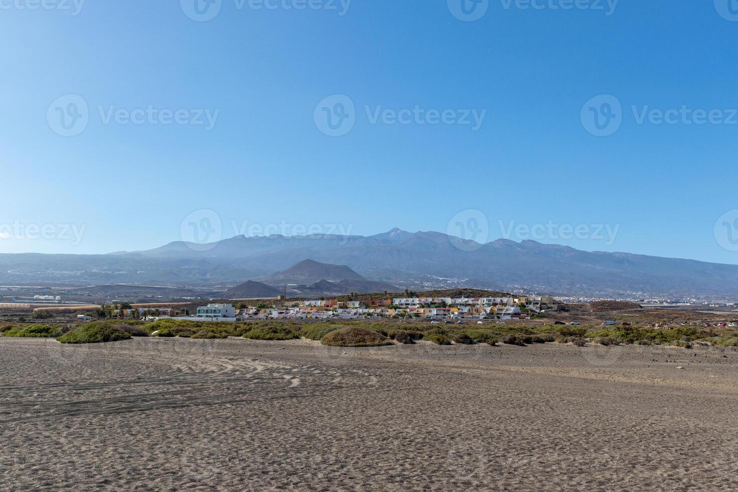 panoramico Visualizza di un' sabbioso spiaggia con un' montagna gamma nel il sfondo sotto un' chiaro blu cielo nel tenerife. foto