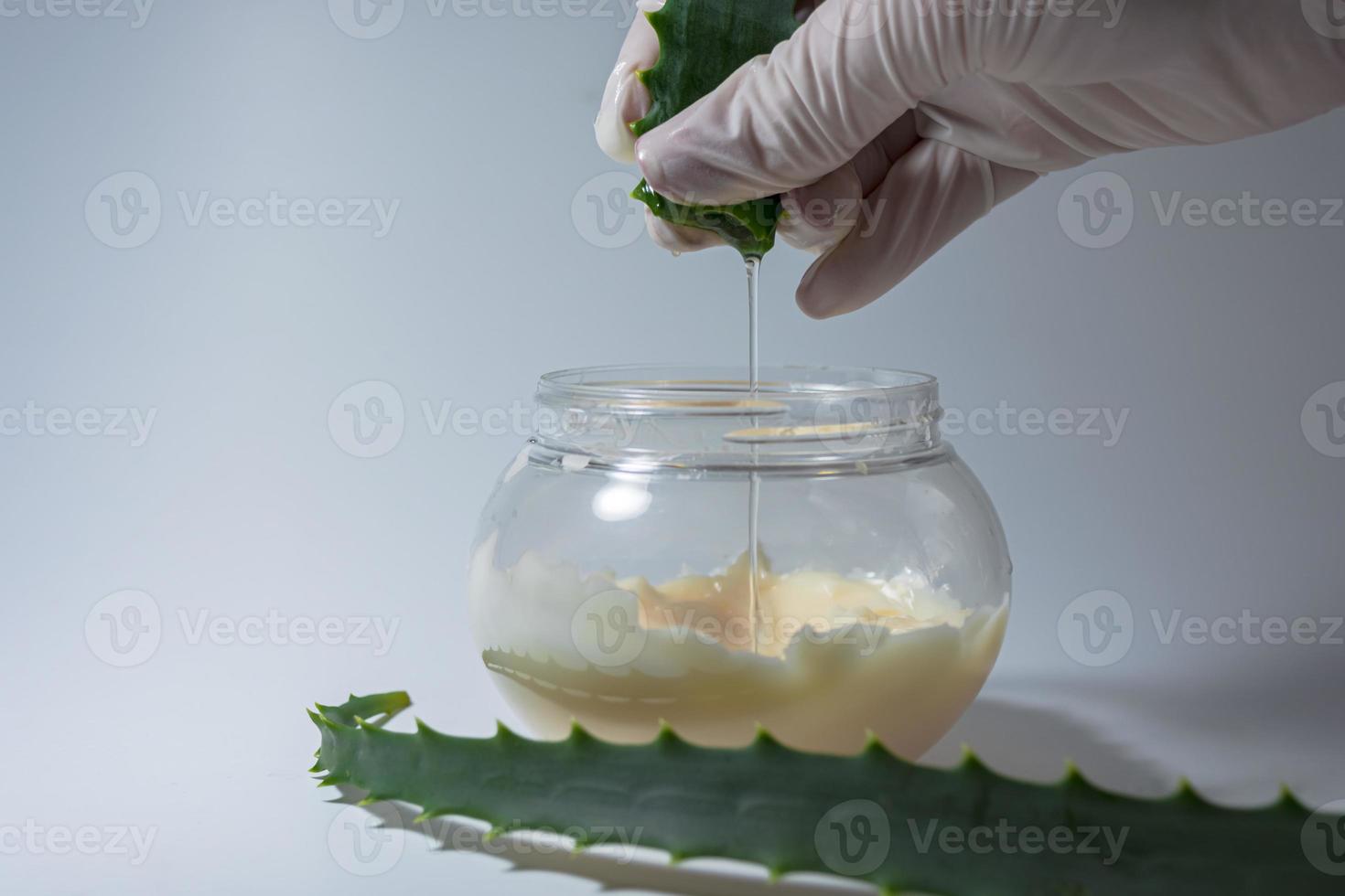 un uomo in guanti bianchi preme il succo di aloe in un barattolo con la panna. foto