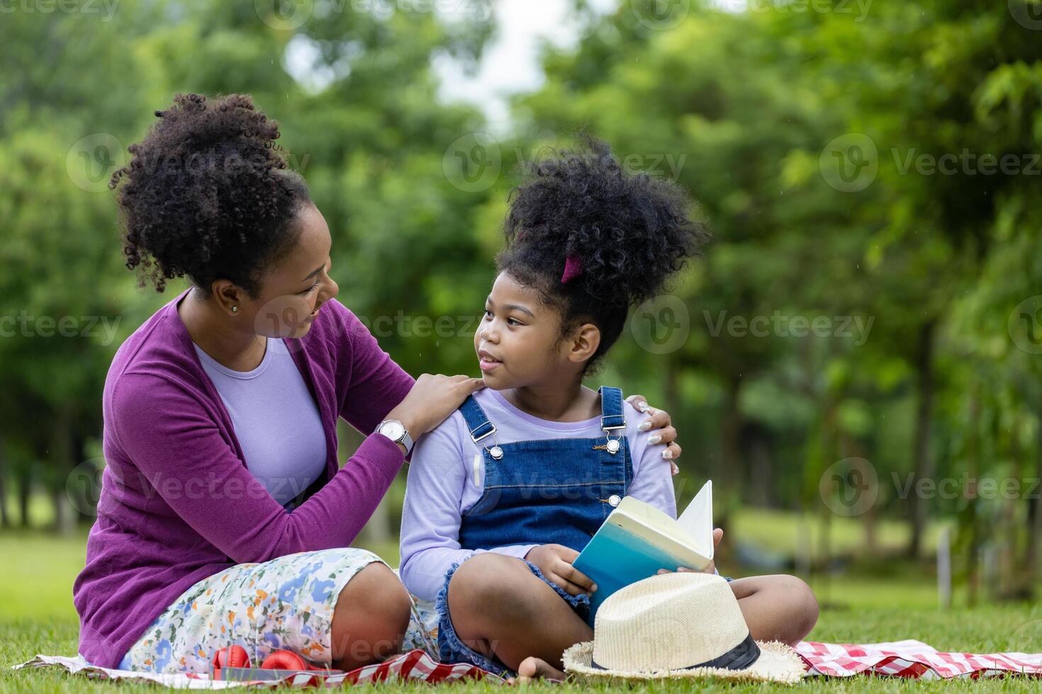africano americano madre è insegnamento sua giovane figlia per leggere mentre avendo un' estate picnic nel il pubblico parco per formazione scolastica e felicità concetto foto