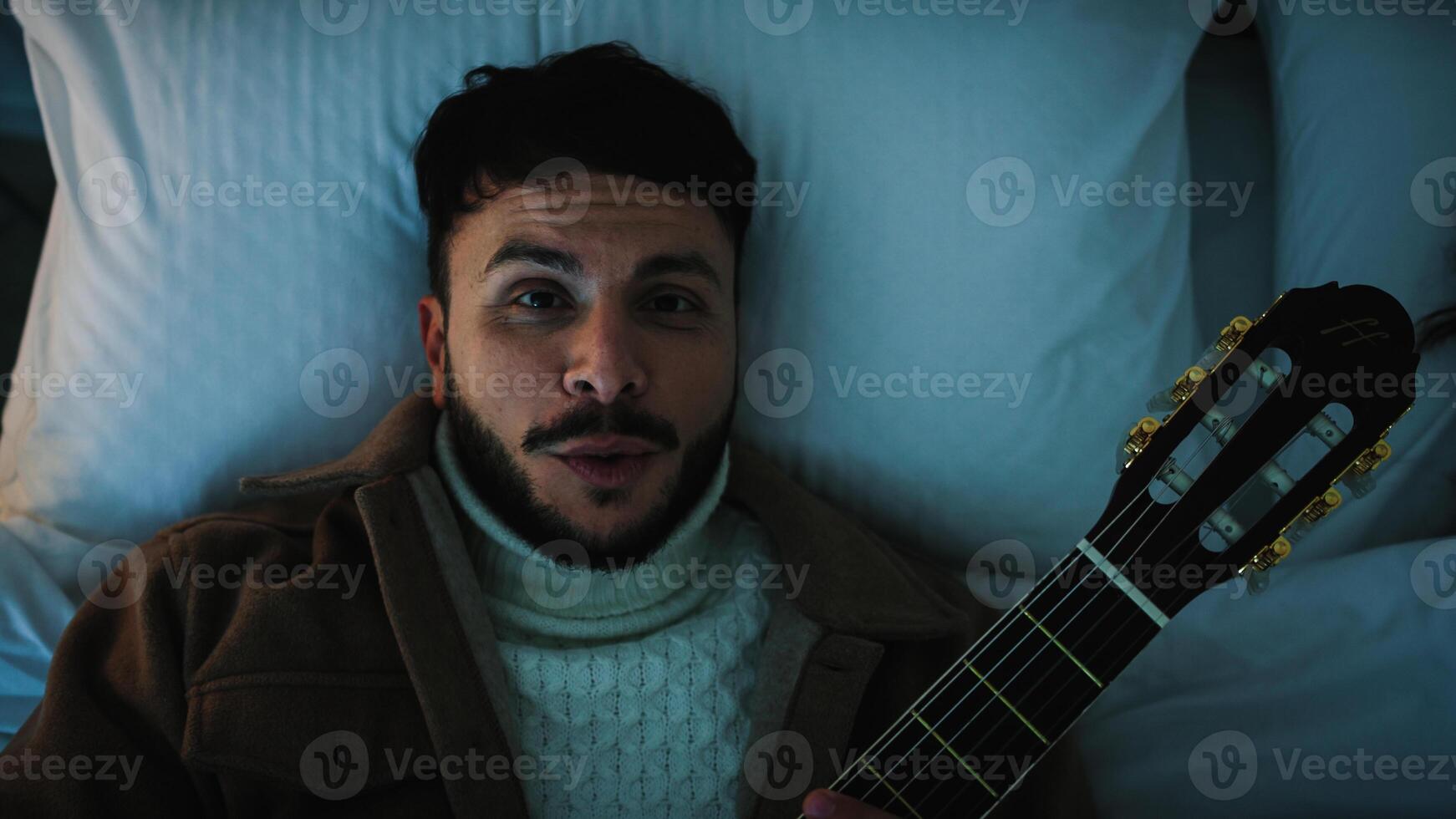 uomo cantare e giocare il chitarra nel un' letto foto