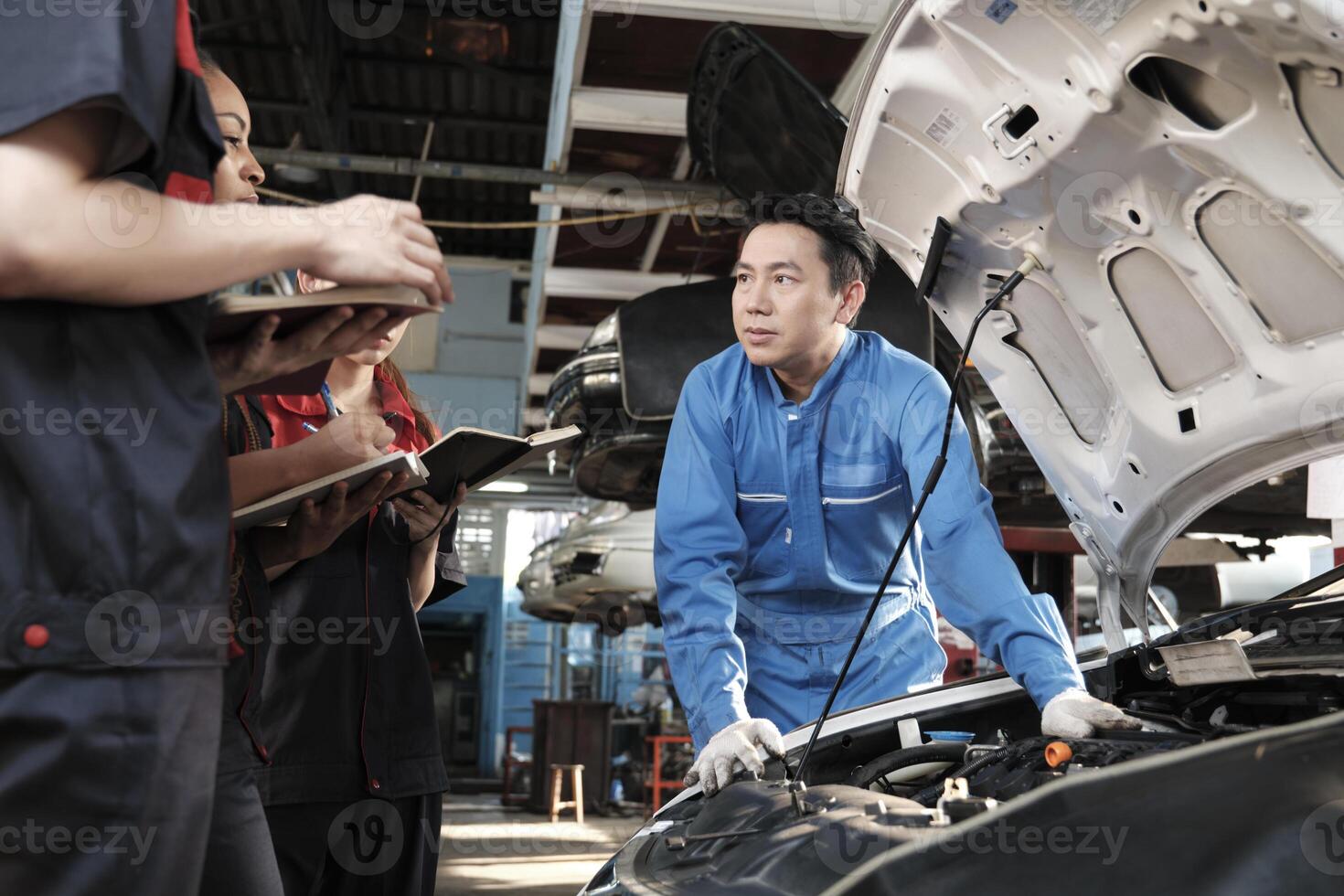 asiatico maschio professionale settore automobilistico ingegnere supervisore descrive auto motore Manutenzione e riparazione opera con meccanico lavoratore personale squadra nel fix servizio box auto, specialista occupazioni nel auto industria. foto