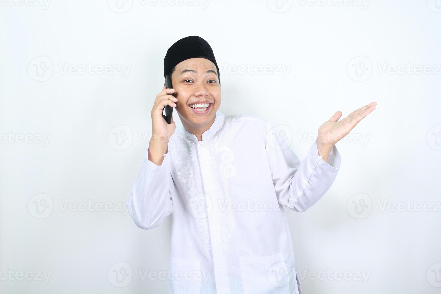 Contentissimo asiatico musulmano uomo presentazione mano per accanto con sorridente viso mentre A proposito di su il suo Telefono isolato foto