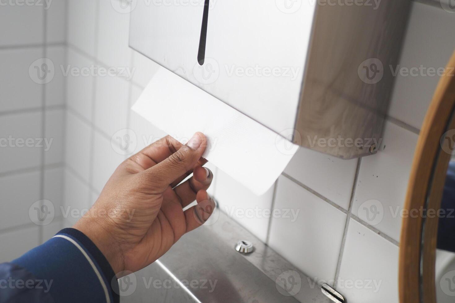 un' persona è utilizzando un' carta asciugamano distributore nel un' bagno foto
