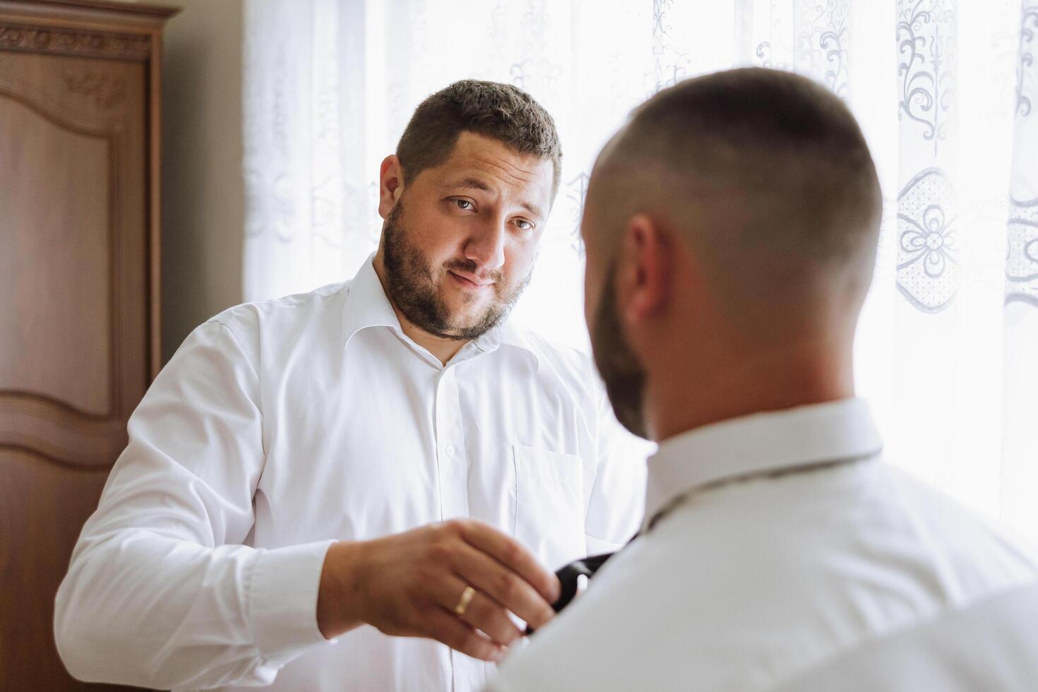 elegante sposo ridendo e avendo divertimento con testimoni dello sposo mentre ottenere pronto nel il mattina per nozze cerimonia. lusso uomo foto