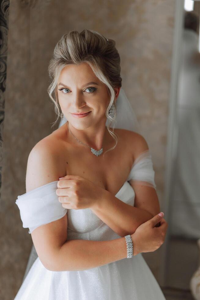 ritratto di il sposa nel il Hotel camera. un' bellissimo giovane ragazza è vestito nel un' bianca nozze vestire. moderno nozze acconciatura. naturale trucco. foto