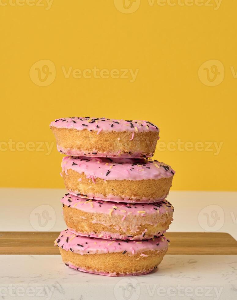 ciambella coperto con rosa Smalto e cosparso con colorato spruzzatori, giallo sfondo foto