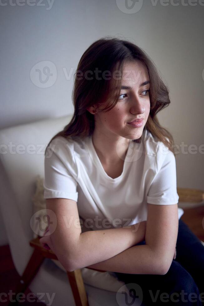 ritratto di un' bellissimo adolescenziale ragazza su un' sedia nel un' luminosa camera nel un' minimalista stile foto