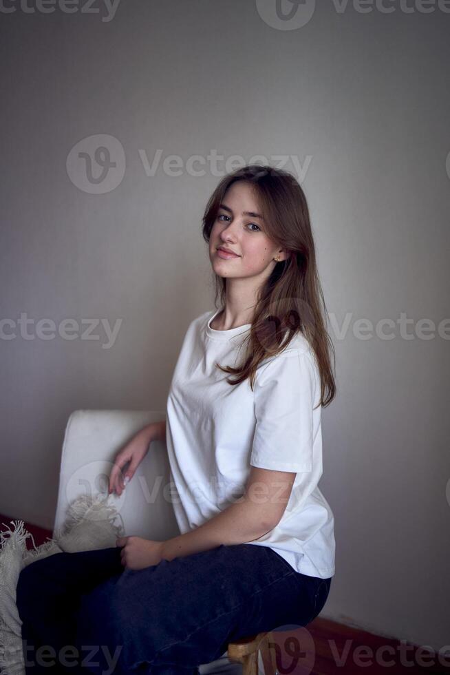 ritratto di un' bellissimo adolescenziale ragazza su un' sedia nel un' luminosa camera nel un' minimalista stile foto