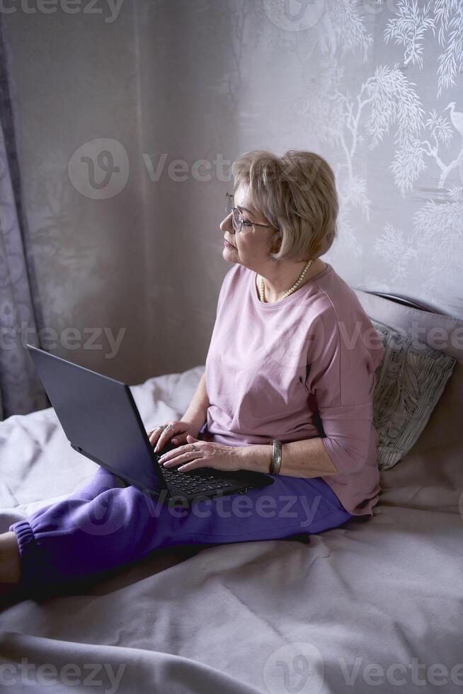 un anziano donna lavori con il computer portatile a casa foto