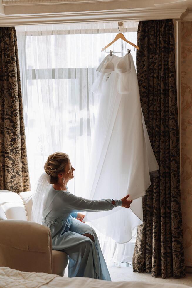 un' bellissimo sposa con un' lungo velo nel sua camera, indossare un' veste. nozze vestito su un' manichino. il sposa nel il mattina prima il nozze cerimonia. foto