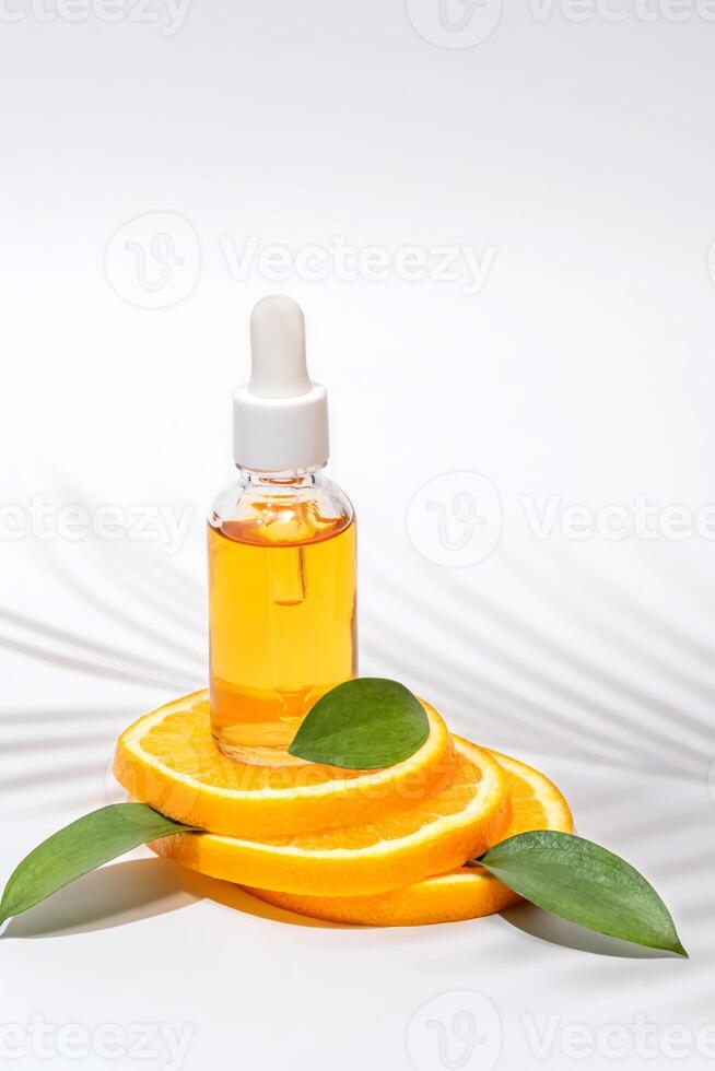 vitamina c siero nel cosmetico bottiglia con contagocce, affettato arancia e verde le foglie su bianca sfondo. biologico terme cosmetici con erbaceo ingredienti. foto