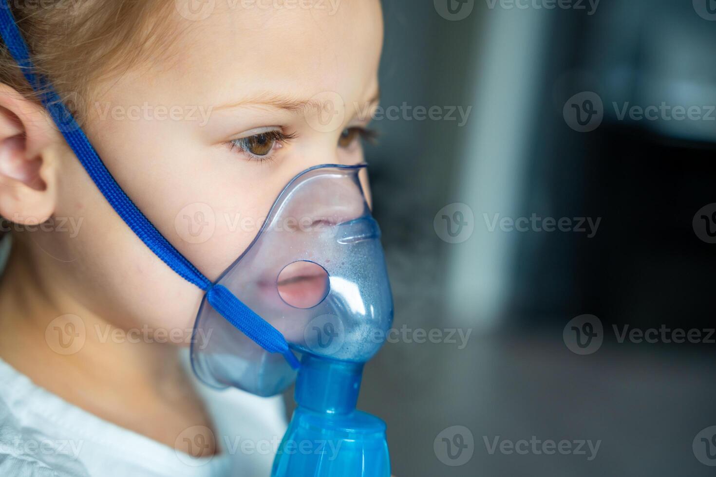 carino poco ragazza siamo seduta e Tenere un' nebulizzatore maschera pendente contro il viso, vie aeree trattamento concetto foto