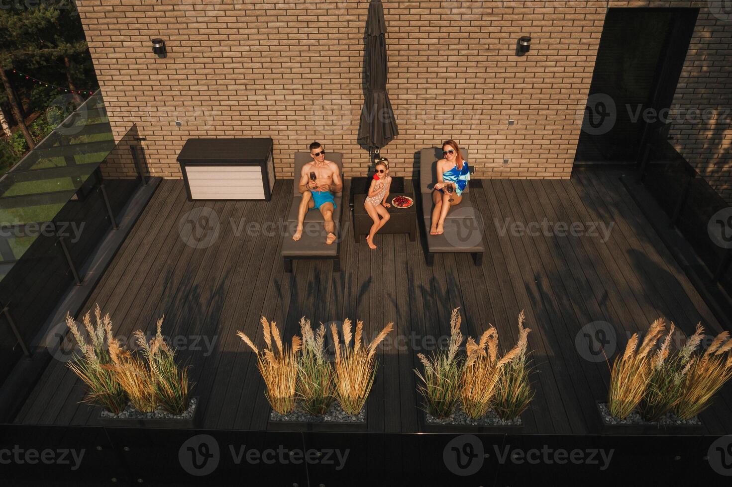 un' contento famiglia nel costumi da bagno prendere il sole nel estate su loro terrazza su sole letti foto