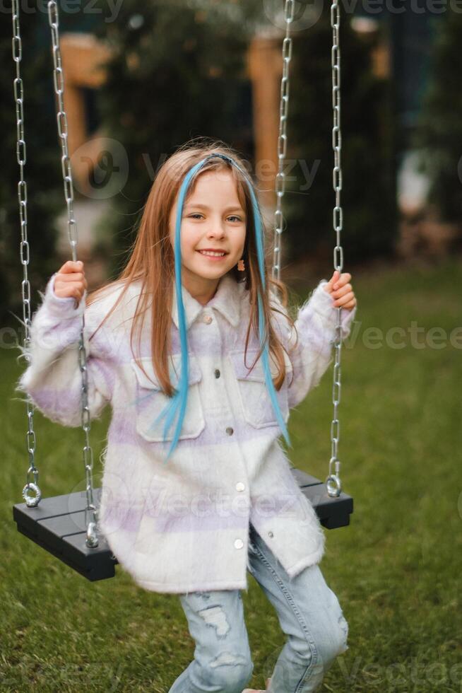 un' bellissimo ragazza con lungo capelli nel un' giacca cavalcate su un' swing nel il sera su il strada foto