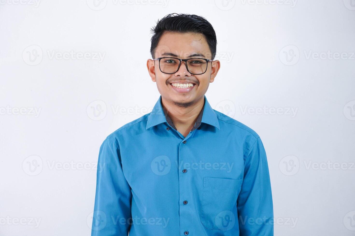 ritratto sorridente o contento asiatico giovane uomo d'affari con bicchieri in piedi e guardare telecamera indossare blu camicia isolato su bianca sfondo foto